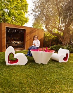 conjunto de muebles en forma de corazon y flores con un chico encima de la mesa riendo